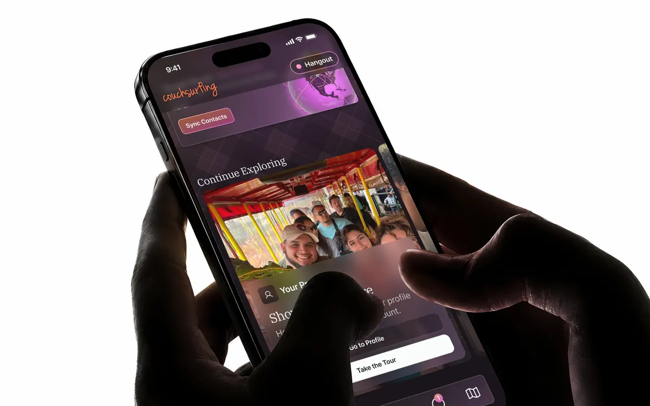 A phone held in two hands, the Couchsurfing Explore screen up: the Continue Exploring row with the Profile tour card, a photo of the member with friends on a tram, and the two buttons, Go to Profile and Take the Tour